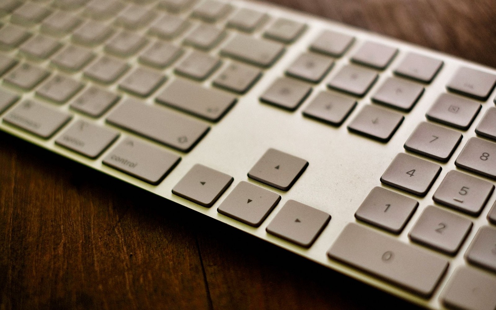 Close-up of a silver keyboard's arrow keys and numeric keypad on a wooden desk