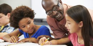 Teacher Helping Pupils Studying At Desks In Classroom